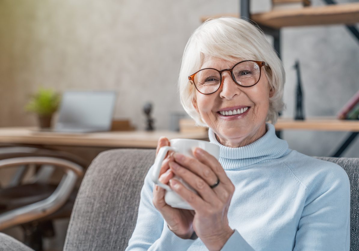 Senior woman drinking hot drink sitting on sofa at home