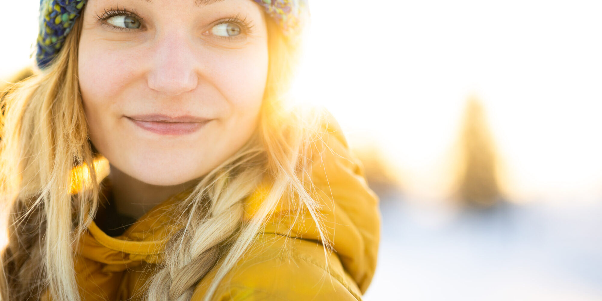 Winter portrait of a pretty, young woman bathing in warm evening sunlight in a snowy landscape.